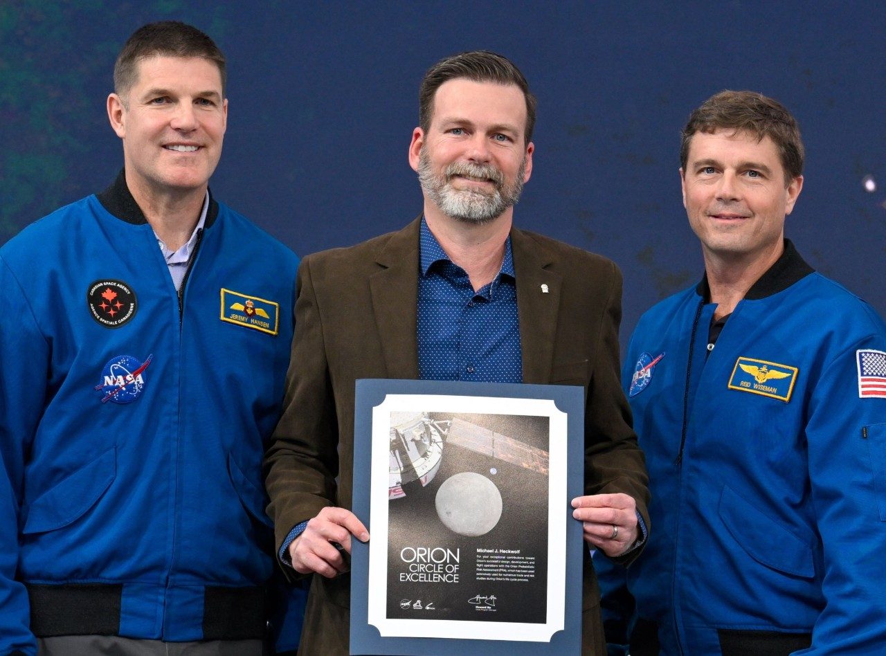 Engineer with Artemis II astronauts posing with Orion picture
