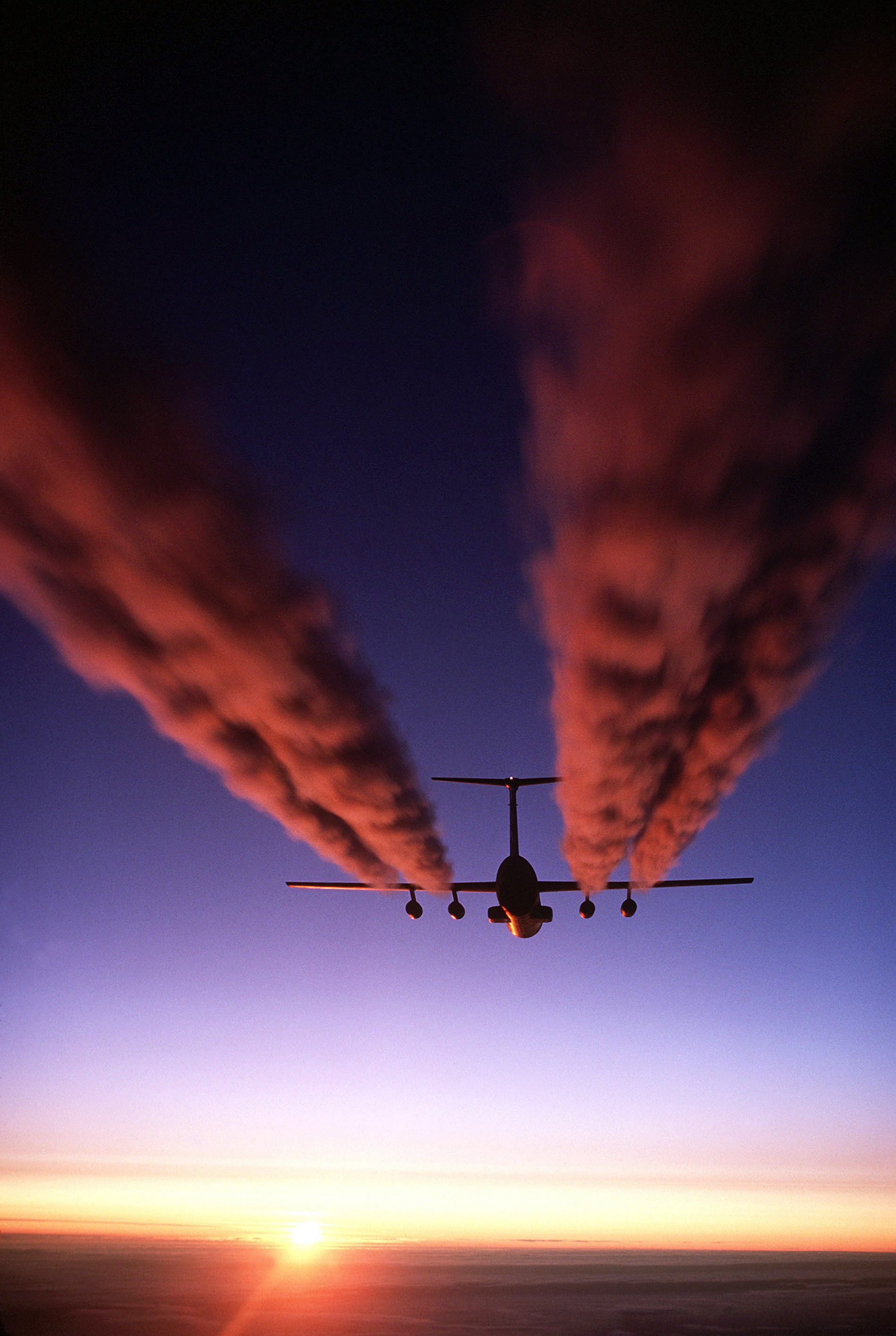 A C-141B Starlifter aircraft leaves four plumes of exhaust behind it as it prepares for an airdrop.