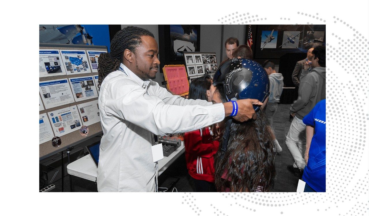 Troy places a helmet on a student visiting the Lockheed Martin facility in Fort Worth, Texas for Junior Achievement Day.