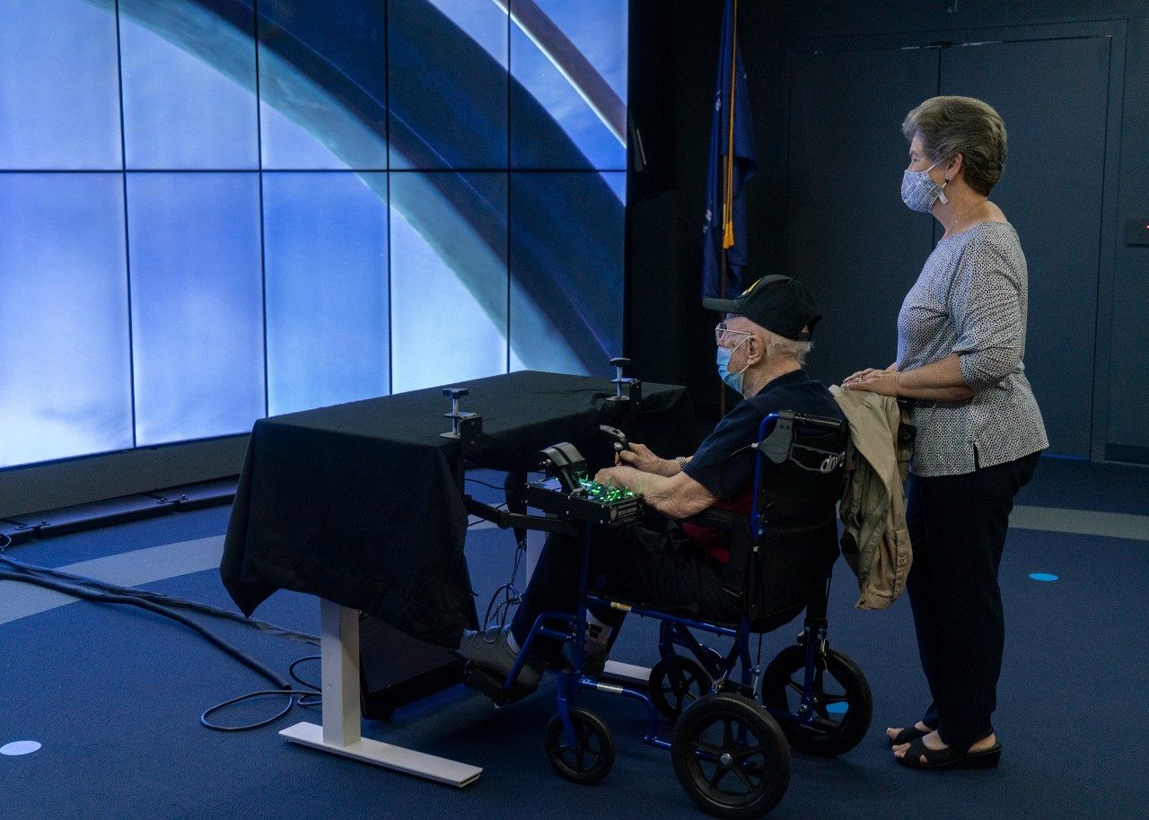 Lockheed Martin recent retiree, Brenda Cook of Orlando watches her father a WWII fighter pilot Charles “Tom” Snead fly the F-35 with Prepar3D simulation and training software.