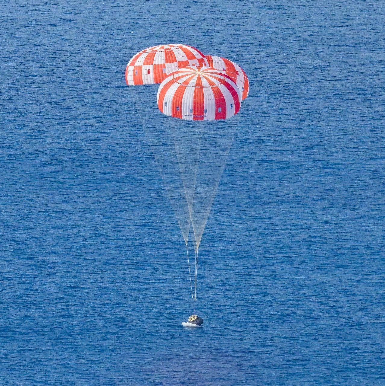 Orion under three opened parachutes splashing down in the Pacific ocean